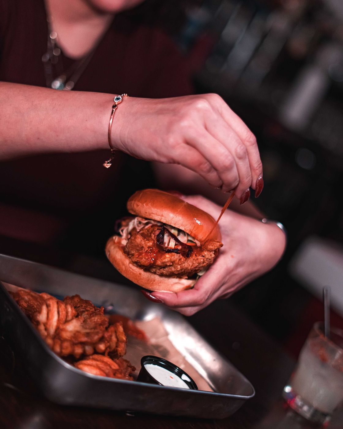Hands holding a fried chicken sandwich over waffle fries