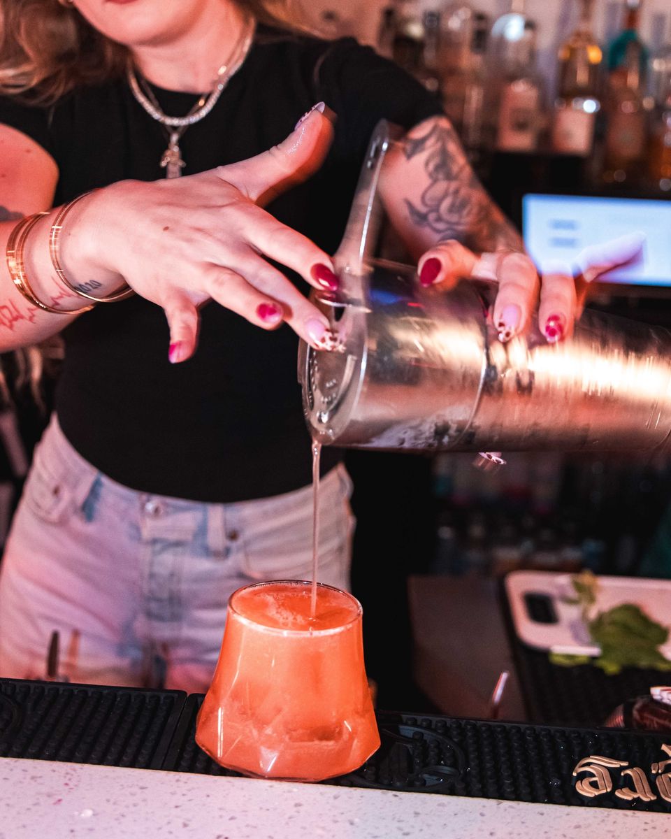 A bartender pouring a cocktail from a shaker
